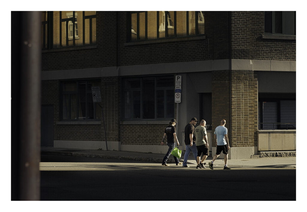 Personnes traversant la rue Quatre hommes traversent une rue au soleil du soir, projetant de longues ombres. Ils se trouvent à côté d'un bâtiment en brique doté de grandes fenêtres. Deux des hommes portent des chemises sombres, un dans une chemise grise et un dans une chemise bleu clair.
